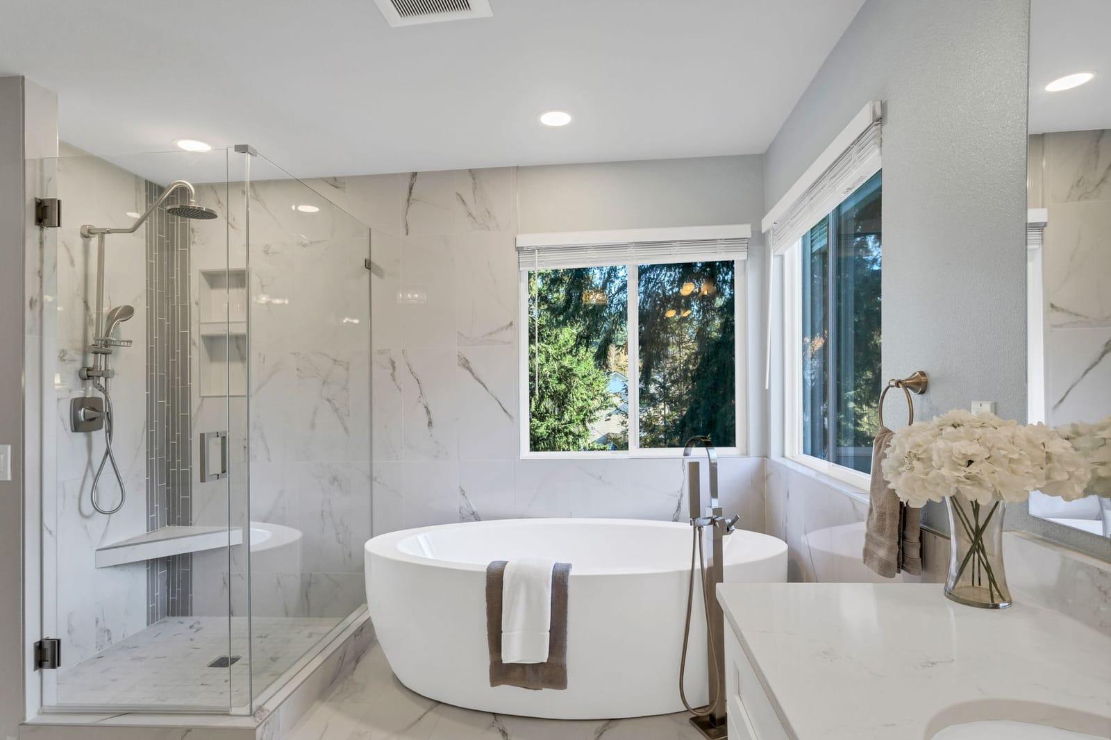 Remodeled master bath with a freestanding soaking tub, glass shower and marble tile