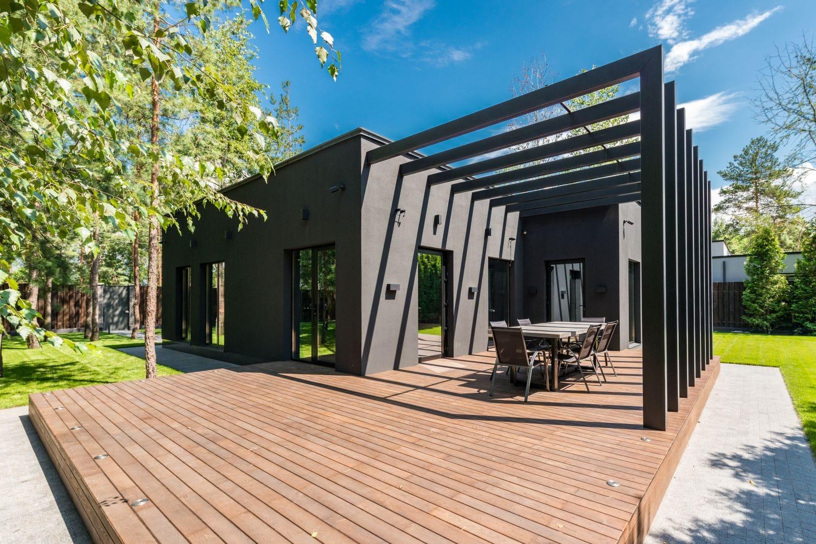 Custom wooden deck with pergola and outdoor dining set beside a modern home